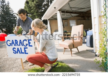 Couple putting up garage sale sign in yard