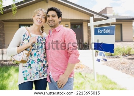 Couple smiling next to For Sale sign