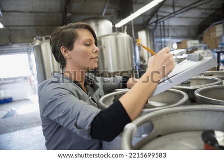 Brewery worker with clipboard leaning on kegs