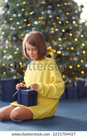              A very cute girl in bright clothes sits and unpacks her Christmas present. New Year                  