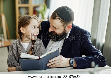 Portrait of smiling jewish father reading book with daughter at home Royalty-Free Stock Photo #2215706541