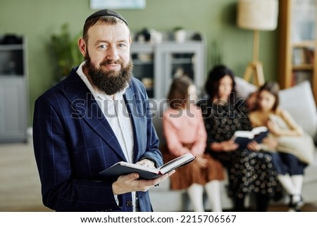 Waist up portrait of bearded jewish man wearing kippah and looking at camera holding book, copy space Royalty-Free Stock Photo #2215706567
