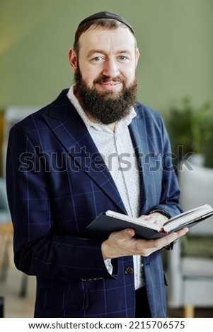 Vertical portrait of bearded jewish man wearing kippah and looking at camera holding book Royalty-Free Stock Photo #2215706575