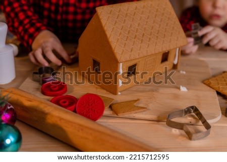 boy and a girl in red christmas pajamas prepare a gingerbread house and decorate it with icing at home in the kitchen. little chefs. High quality photo
