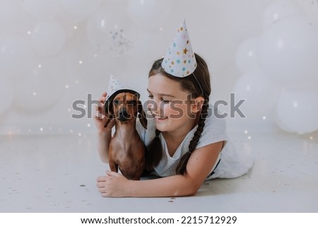 little brunette girl and her favorite dog dachshund in festive hats lie on the floor in front of the camera. girl celebrates her birthday. High quality photo