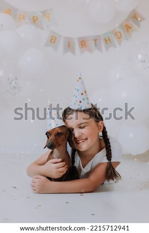 little brunette girl and her favorite dog dachshund in festive hats lie on the floor in front of the camera. girl celebrates her birthday. High quality photo