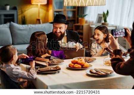 Portrait of modern jewish family sharing gifts at dinner table in cozy home setting