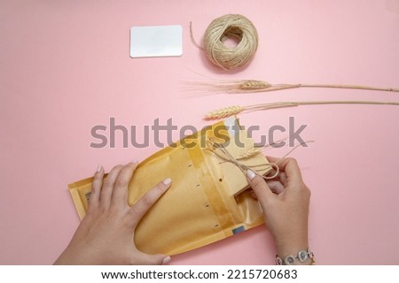 Preparing  package, sending set for an on-line entrepreneur seller with pink background, a white card, a wheat branch, a paperboard envelope, and a ball of rope