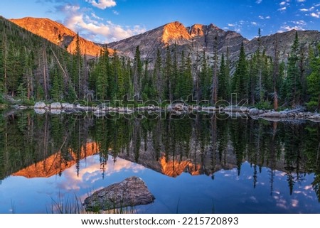 Ypsilon Mountain and Mount Chiquita are reflected in the calm water of Chipmunk Lake with the first light of golden hour in Rocky Mountain National Park, Colorado. Royalty-Free Stock Photo #2215720893