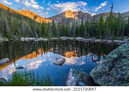 Boulders surround the calm water of Chipmunk Lake reflecting Ypsilon Mountain and Mount Chiquita lit by morning light in Rocky Mountain National Park, Colorado. Royalty-Free Stock Photo #2215720897