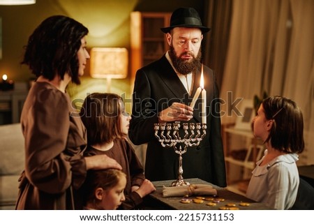 Portrait of orthodox jewish man with family lighting menorah candle during Hanukkah celebration