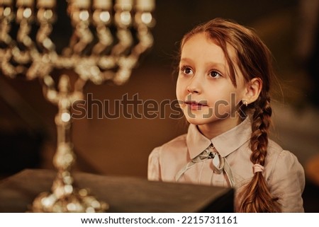 Portrait of cute jewish girl looking at menorah candle during Hanukkah celebrations Royalty-Free Stock Photo #2215731161
