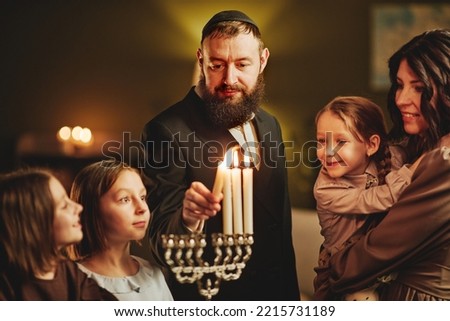Portrait of orthodox jewish man lighting menorah candle with family during Hanukkah celebration Royalty-Free Stock Photo #2215731189