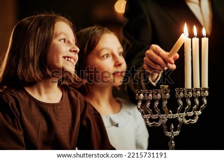Side view portrait of two jewish girls looking at Menorah candle and smiling happily during Hanukkah celebration, copy space