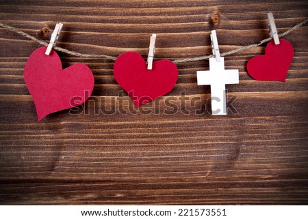 On A Wooden Background Hanging red Hearts and a white Cross on a Line
