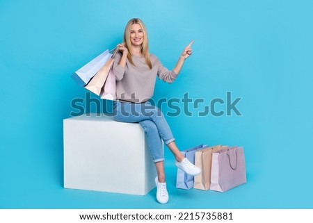 Full length photo of shiny sweet girl dressed grey sweatshirt sitting white platform holding bargains empty space isolated blue color background