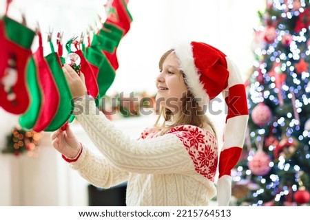 Kids opening Christmas presents. Child searching for candy and gifts in stocking advent calendar on winter morning. Decorated Christmas tree for family with children. Xmas fun.