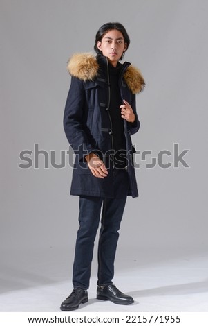 fashion model. full body young man in black fur coat posing in studio on gray background