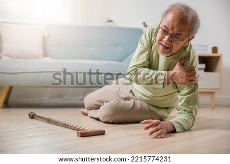 Sick senior old man falling down lying on the ground because stumbled at home alone with wooden walking stick in living room, elderly man grandfather having accident while walk with cane walker Royalty-Free Stock Photo #2215774231