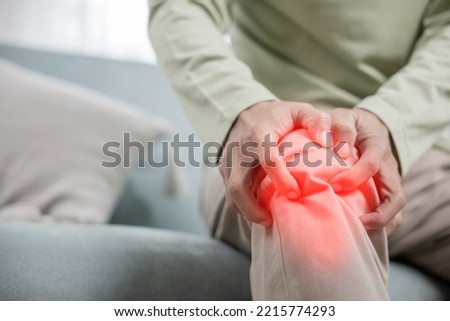 Old man suffering from knee joint pain on sofa living room, bone pain in elderly at home, senior man knee problem painful, unhappy old age hand holding on knee pain after tendon surgery Royalty-Free Stock Photo #2215774293