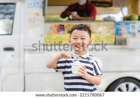 portrait happy kid Thai boy eating coconut ice cream milk with a smile on food ice cream truck background. funny kid Korean boy child eats icecream coconut in the summer in Thailand.food truck people.