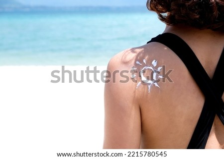 A woman is applying sunscreen and skin care to protect her skin from UV rays. She is applying sunscreen on her back, the sun sign. Health and skin care concept Royalty-Free Stock Photo #2215780545