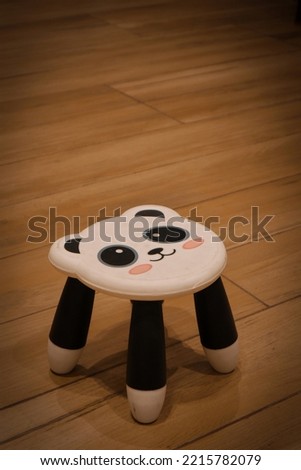 panda face plastic stool with 3 legs for kids against wooden floor. copy space
