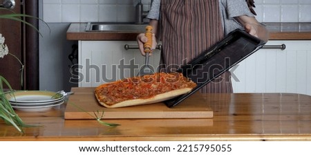 A young boy in an apron demonstrates a pizza prepared at home against the background of a kitchen cabinet. Healthy homemade food.