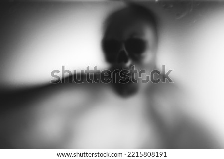 Horror skeleton or grim reaper behind the matte glass. Halloween festival concept.Blurred picture