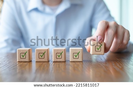 Checklist, Task list, Survey and assessment, Quality Control, Goals achievement and business success. Vote, to do list, Hand holding green check mark on wooden block to complete checklist.
