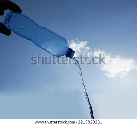 Mineral  water flowing from a transparent plastic bottle on blue cloudy sky background. Bottle with drinking water blue background with clouds. Fresh water in plastic cup. empty Copy space.