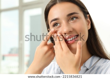 Woman putting contact lens in her eye at home Royalty-Free Stock Photo #2215836821