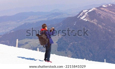 Happy lifestyle with tourist blogger travel with snow peak view and  taking photo by smartphone with snow  alpine mountain at Switzerland with blue sky background