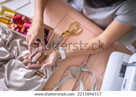 Woman dressmaker hands choosing thread color for sewing beige fabric clothes at workshop studio closeup. Female tailor fashion designer art work modist dressmaking professional occupation top view Royalty-Free Stock Photo #2215846517