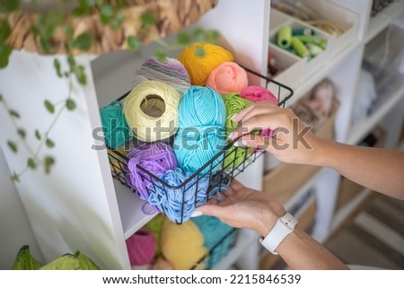Female hands placing basket with colored ball of yarn for art crochet knitting ribbon cotton wool thread for hobby. Woman tailor sewing materials comfortable storage cupboard arrangement organize Royalty-Free Stock Photo #2215846539
