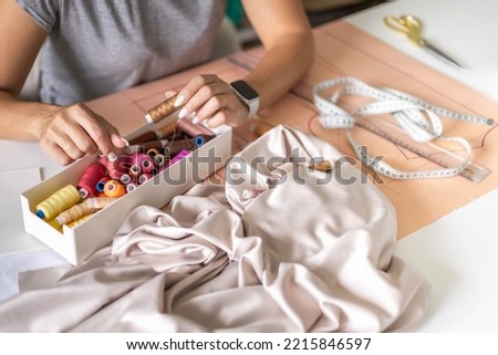 Woman dressmaker hands choosing thread color for sewing beige fabric clothes at workshop studio closeup. Female tailor fashion designer art work modist dressmaking professional occupation top view Royalty-Free Stock Photo #2215846597