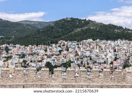 View of Kavala chaotic urban residential development on a forested hill through the battlements of the castle masonry wall on the top of the old cape