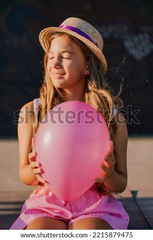 Portrait of a girl in a hat with a pink balloon. She is dressed in pink clothes and her hair is long and loose.