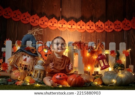 

Cute small baby is staying near a lot of pumpkins in at autumn and halloween decorated scenography. Studio photography.