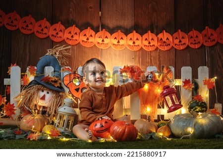 

Cute small baby is staying near a lot of pumpkins in at autumn and halloween decorated scenography. Studio photography.