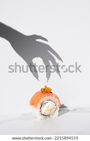 Sushi Halloween on white background. Maki roll with witch hand shadow. Creative party food. Spooky, scary, fun, bewitched California with salmon. Japanese sushi bar, restaurant holiday menu. Vertical