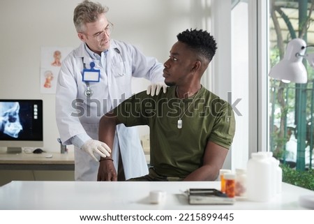 Doctor palpating dislocated shoulder of soldier in medical office Royalty-Free Stock Photo #2215899445