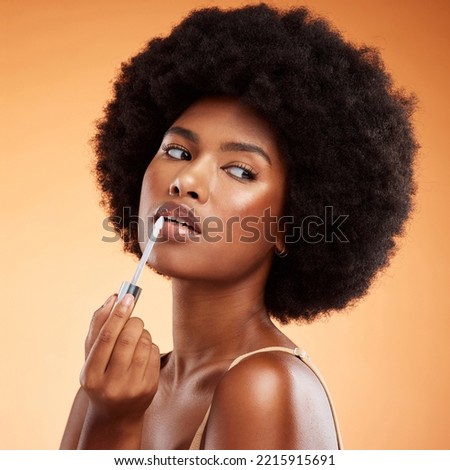Black woman, afro and natural beauty lip gloss treatment for a healthy, shiny and transparent tint. Cosmetics, apply and beautiful face of African model holding makeup tool at orange background. Royalty-Free Stock Photo #2215915691