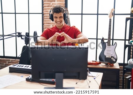 Young hispanic man playing piano keyboard at music studio smiling in love showing heart symbol and shape with hands. romantic concept. 