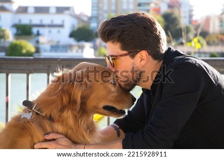 young latino man and his brown golden retriever dog walking in the street. The man kisses the dog on the head with affection. Concept pets, animals, dogs, pet love, golden retriever. Royalty-Free Stock Photo #2215928911