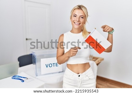 Young caucasian woman at political campaign election holding poland flag smiling happy pointing with hand and finger 
