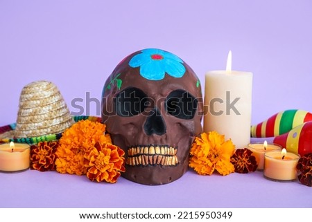 Painted skull for Mexico's Day of the Dead (El Dia de Muertos), flowers, candles and sombrero hat on lilac background