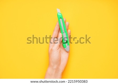 Man with utility knife on yellow background, closeup