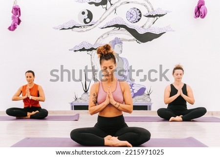 three women practicing yoga and meditation on their mats in a studio. yoga teacher giving class