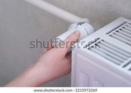 Rising heating costs in the crisis: man or woman, person regulates the temperature at home with the heating thermostat to save energy, close up photo with hand. Hand turns the battery heating knob